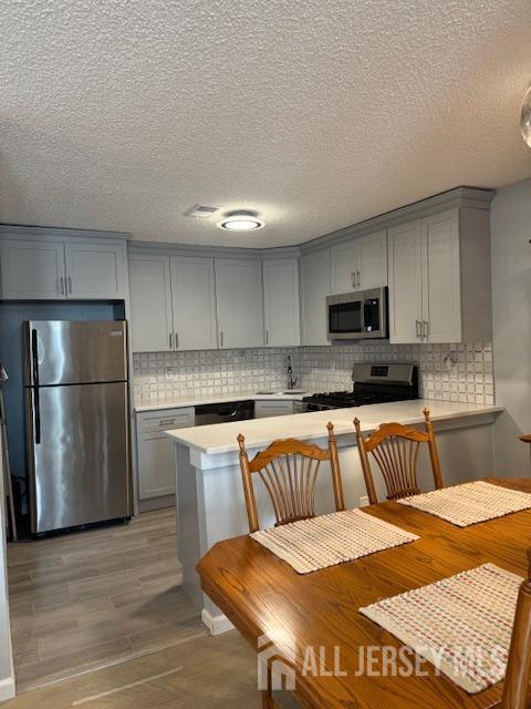 kitchen featuring appliances with stainless steel finishes, gray cabinetry, kitchen peninsula, and light wood-type flooring