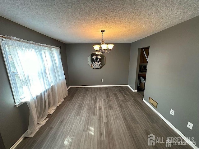 unfurnished dining area featuring a chandelier, a textured ceiling, dark wood finished floors, and baseboards