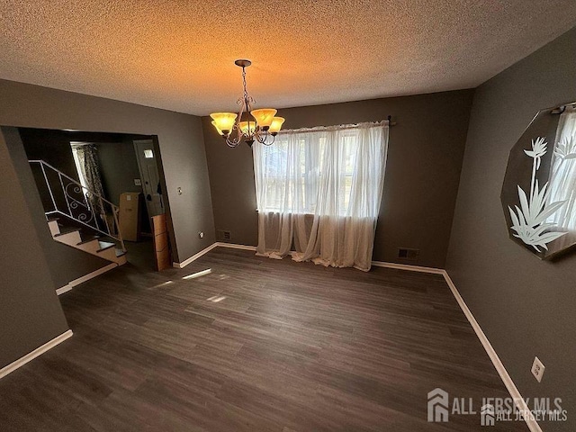 unfurnished dining area with baseboards, dark wood-style floors, stairs, a textured ceiling, and a notable chandelier