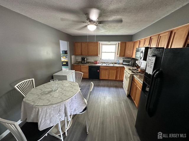 kitchen with decorative backsplash, brown cabinets, dark wood-style flooring, black appliances, and a sink