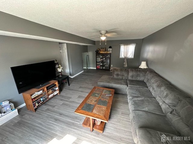 living room with ceiling fan, a textured ceiling, baseboards, and wood finished floors