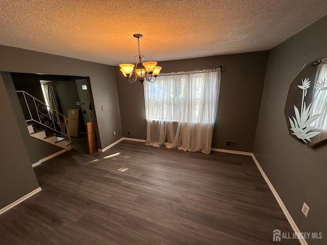 unfurnished dining area featuring dark hardwood / wood-style flooring, a textured ceiling, and a chandelier