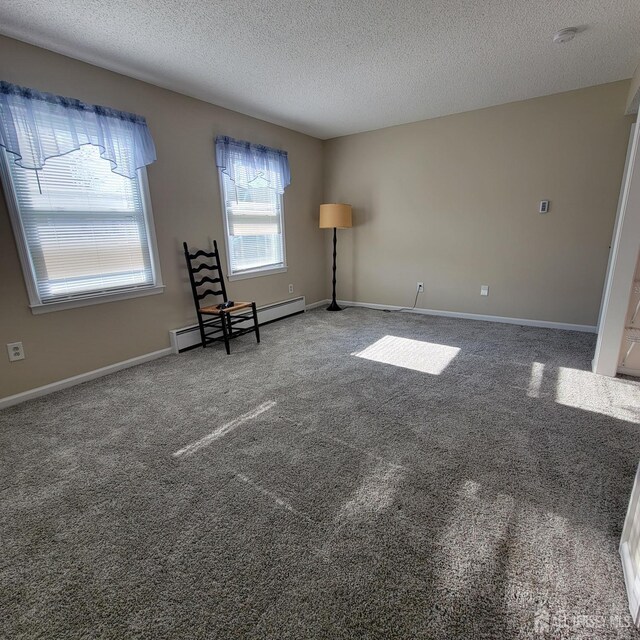 spare room with a textured ceiling, carpet floors, and a baseboard heating unit