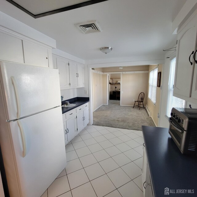 kitchen with white refrigerator, light colored carpet, a baseboard radiator, and white cabinetry