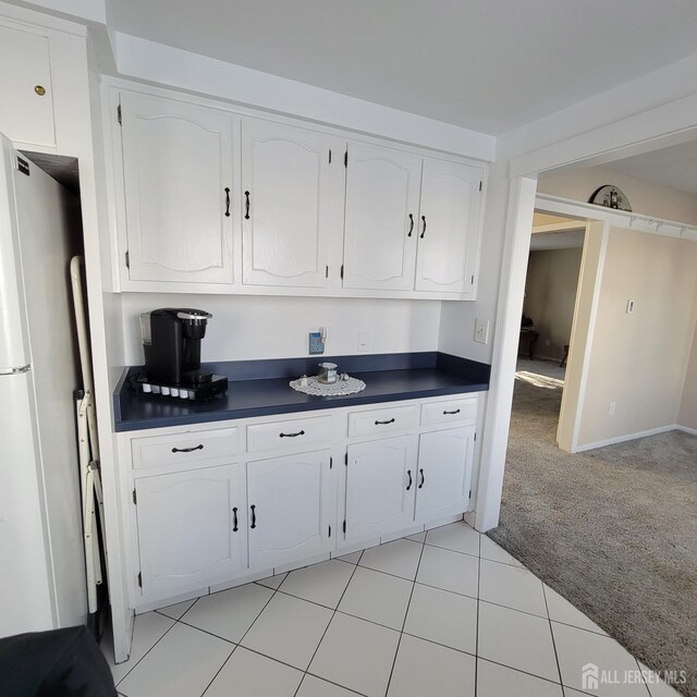 kitchen featuring white refrigerator, white cabinetry, and light carpet