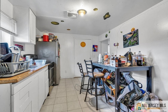 kitchen with gas stove, white cabinetry, light countertops, and light tile patterned flooring