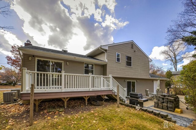 back of house featuring a lawn, an outdoor fire pit, central air condition unit, a wooden deck, and a patio area