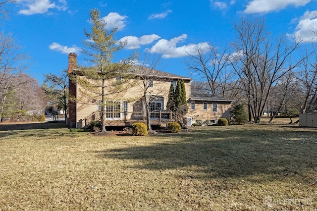 back of house featuring a chimney, a deck, and a lawn