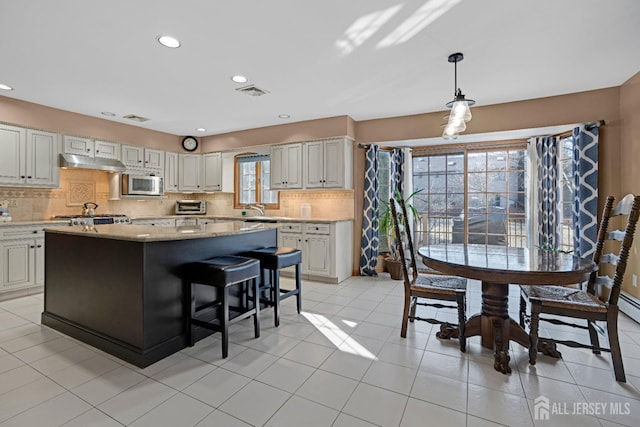 kitchen featuring hanging light fixtures, stainless steel microwave, a center island, and under cabinet range hood