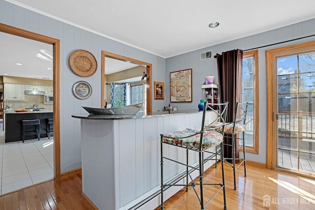 kitchen featuring visible vents, white cabinets, a peninsula, light wood-type flooring, and under cabinet range hood