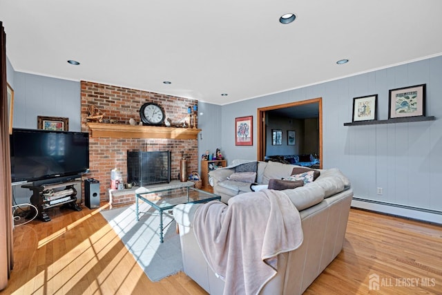 living room featuring baseboard heating, a fireplace, light wood-style flooring, and crown molding