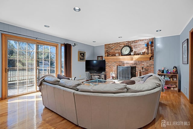 living room featuring a brick fireplace, crown molding, light wood-style floors, and recessed lighting