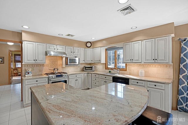 kitchen featuring visible vents, light stone countertops, stainless steel appliances, under cabinet range hood, and a sink