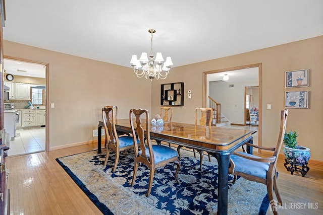 dining room featuring baseboards, light wood-type flooring, stairs, and an inviting chandelier