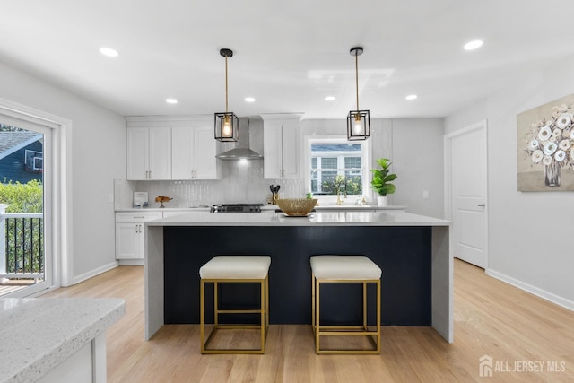 39 S Pierson Rd, Maplewood, NJ 07040 - kitchen with wall chimney exhaust hood, a center island, white cabinetry, light wood-style floors, and light countertops