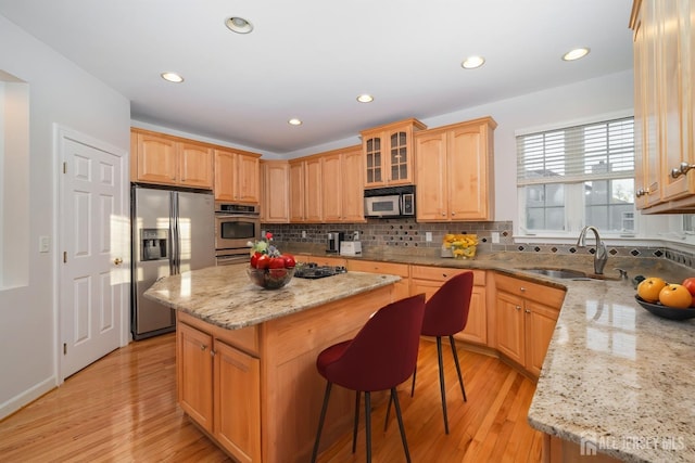 kitchen with light stone counters, a sink, stainless steel appliances, backsplash, and a center island