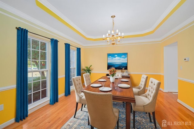 dining area with baseboards, a raised ceiling, an inviting chandelier, and wood finished floors