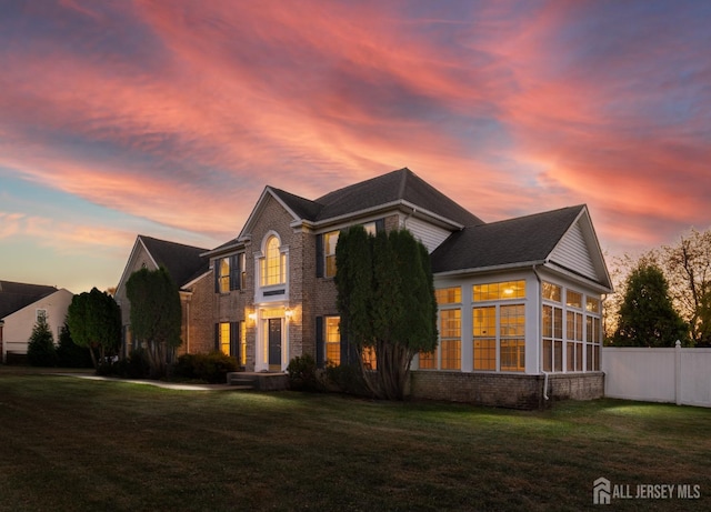 view of front of house with a front yard, fence, brick siding, and a sunroom