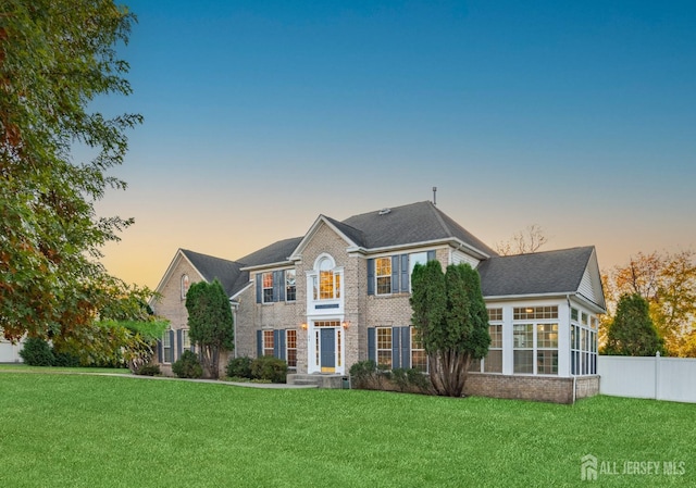 view of front of property featuring fence, brick siding, and a lawn