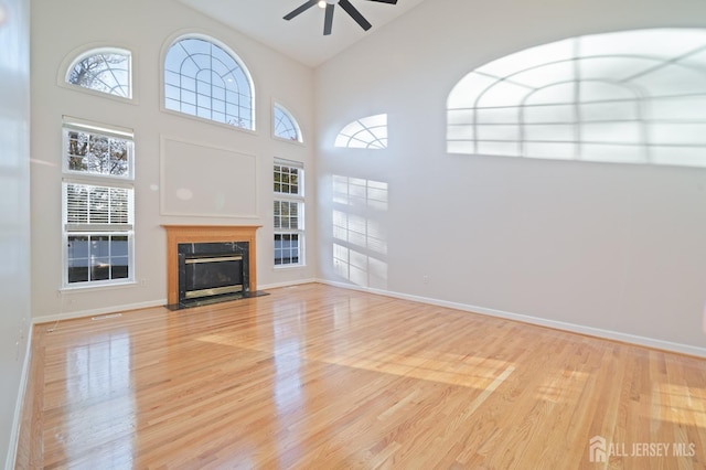 unfurnished living room featuring ceiling fan, light wood-style floors, baseboards, and a premium fireplace