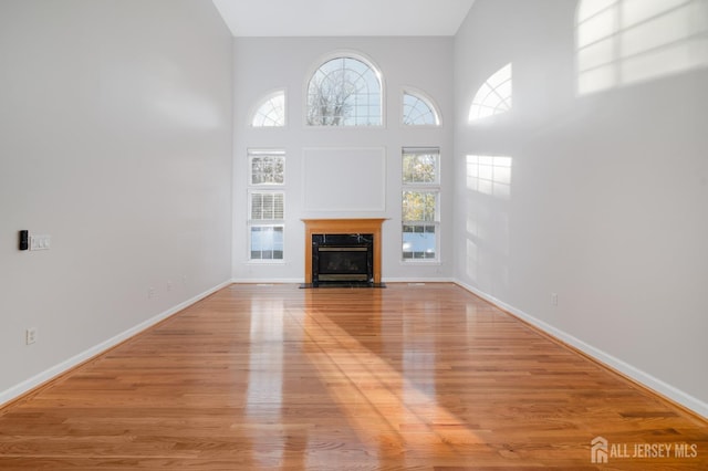 unfurnished living room with light wood-style flooring, a towering ceiling, baseboards, and a high end fireplace