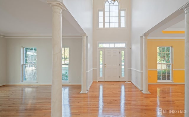 foyer featuring light wood finished floors, a wealth of natural light, crown molding, and ornate columns