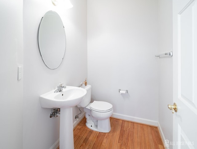 half bath with toilet, wood finished floors, and baseboards