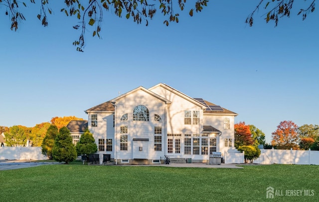 back of house featuring solar panels, a patio, a yard, and fence