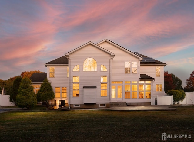 back of house at dusk with solar panels, fence, entry steps, a yard, and a patio area