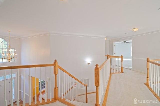 corridor featuring visible vents, an upstairs landing, carpet flooring, crown molding, and a chandelier