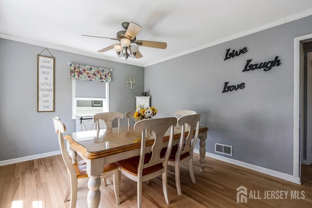 dining room with ceiling fan, baseboards, wood finished floors, visible vents, and ornamental molding