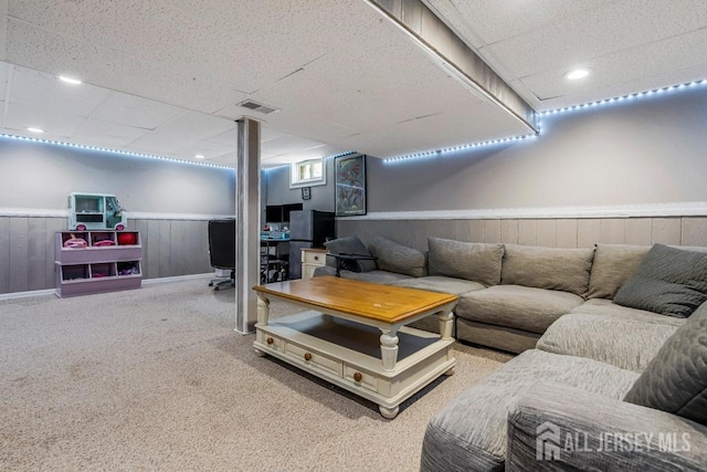 living room with a wainscoted wall, a drop ceiling, carpet floors, and visible vents