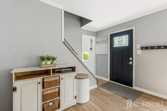 foyer entrance with light wood-style floors, ornamental molding, and baseboards