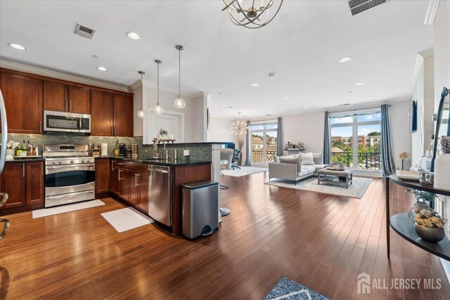 kitchen with appliances with stainless steel finishes, a chandelier, crown molding, tasteful backsplash, and dark wood finished floors