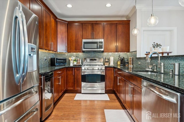 kitchen featuring appliances with stainless steel finishes, a sink, crown molding, dark stone countertops, and decorative backsplash