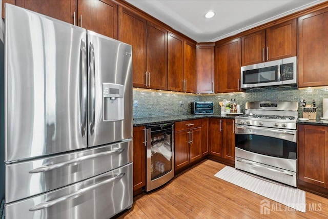 kitchen featuring appliances with stainless steel finishes, beverage cooler, light wood-style floors, dark stone countertops, and backsplash