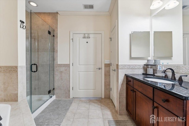 full bathroom featuring tile walls, a shower stall, crown molding, a wainscoted wall, and tile patterned floors