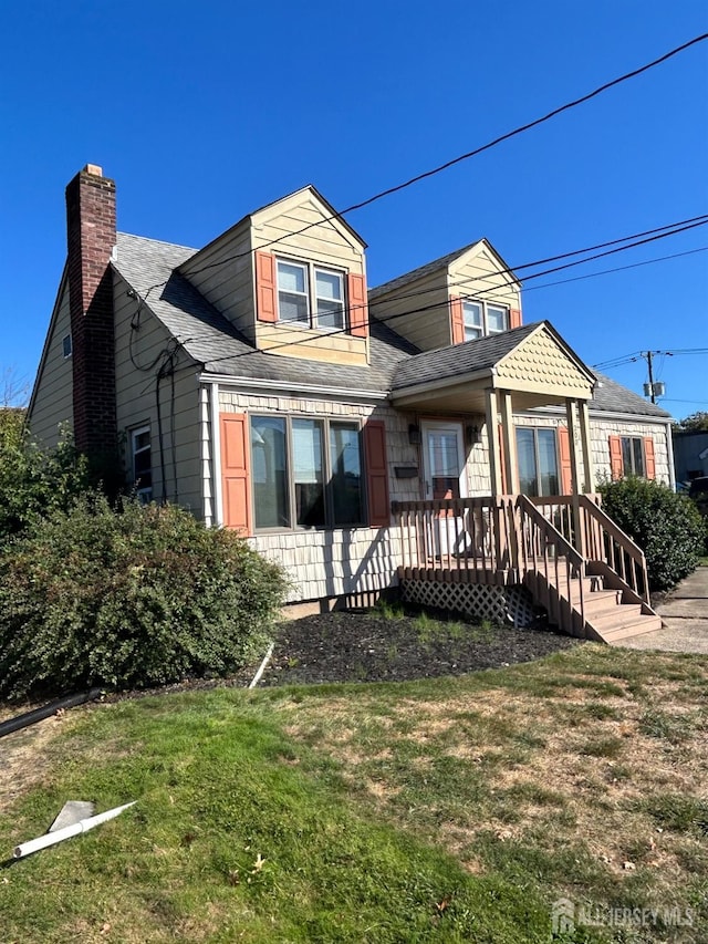 view of front facade with a chimney, a front lawn, and roof with shingles