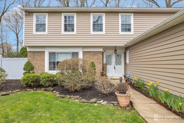 property entrance featuring a lawn, brick siding, and fence