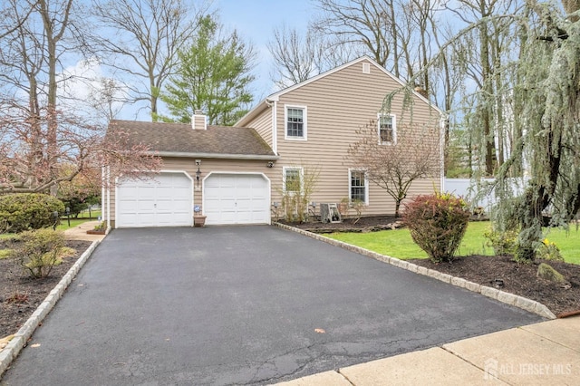 view of home's exterior featuring aphalt driveway, roof with shingles, a garage, and a chimney