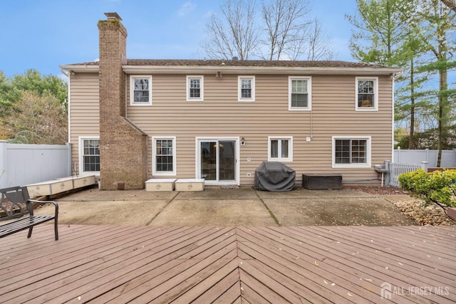 rear view of house featuring a fenced backyard, a wooden deck, a patio, and a chimney