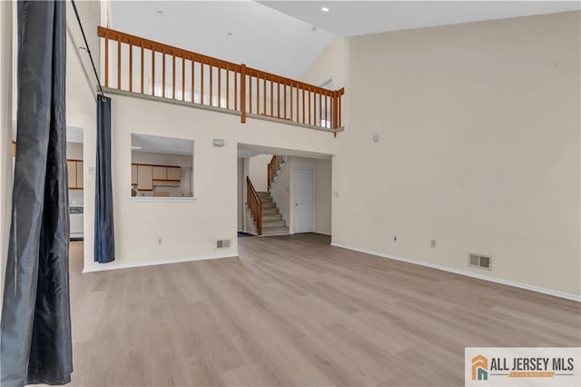 unfurnished living room featuring stairs, baseboards, visible vents, and light wood finished floors