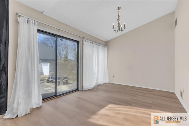 empty room featuring wood finished floors, baseboards, visible vents, an inviting chandelier, and lofted ceiling