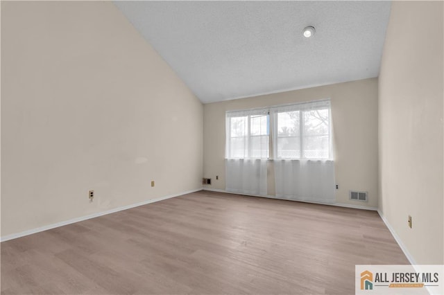 empty room featuring baseboards, visible vents, lofted ceiling, light wood-style floors, and a textured ceiling