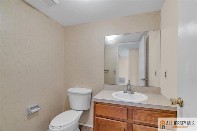 half bath with wallpapered walls, toilet, and vanity