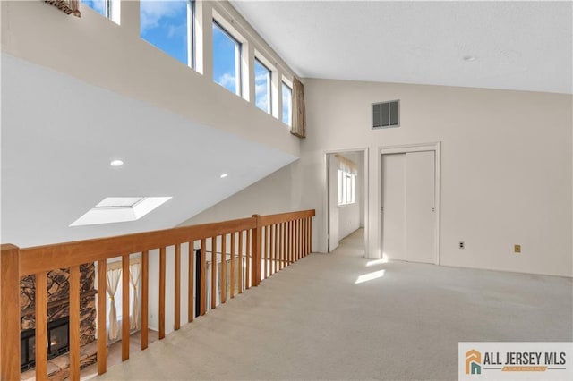 interior space featuring a skylight, visible vents, high vaulted ceiling, and carpet floors