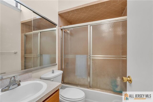 bathroom with toilet, vanity, and bath / shower combo with glass door