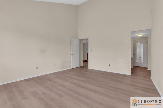 unfurnished room featuring light wood finished floors, baseboards, and a towering ceiling