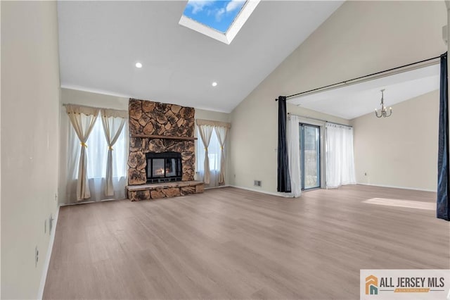 unfurnished living room with a stone fireplace, a skylight, wood finished floors, and a chandelier