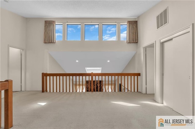 hall featuring carpet, visible vents, a towering ceiling, and a textured ceiling